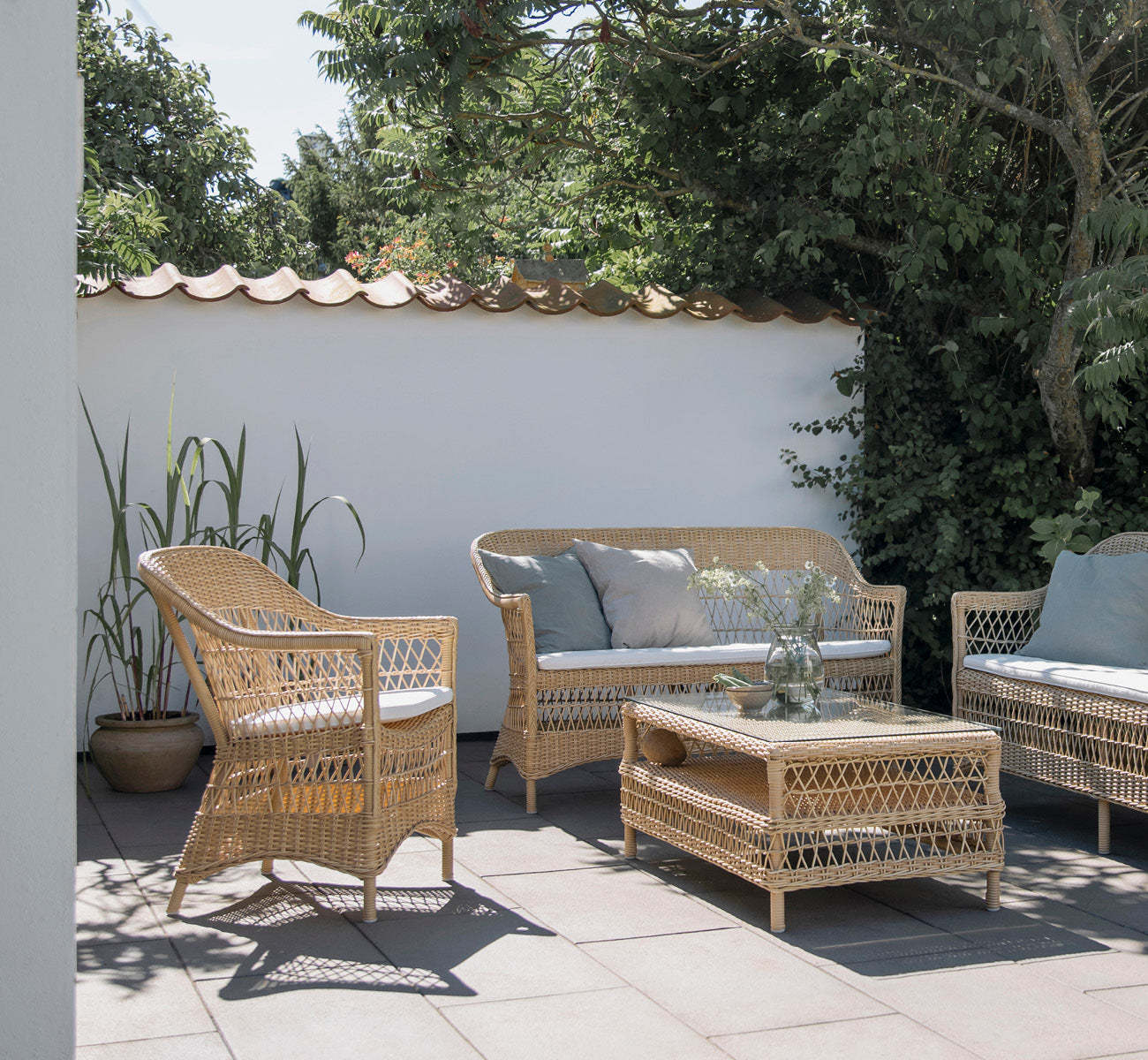 Dies ist ein Lifestyle-Bild von Hazel Couchtisch in natural ArtFibre Aluminium, auf einer schattigen Küstenterrasse mit Schilfdach und Meerblick.