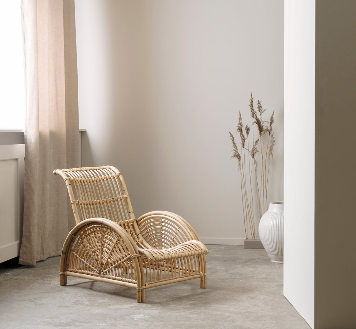 Dies ist ein Lifestyle-Bild von Paris Lounge-Sessel in polished natural rattan. Auf einem Fischgrätparkettboden neben einer passenden Bank platziert.
