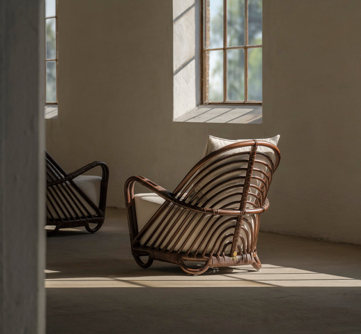 Dies ist ein Lifestyle-Bild von Charlottenborg Lounge-Sessel in brown rattan. Paar im weichen Fensterlicht mit tiefen Schatten.