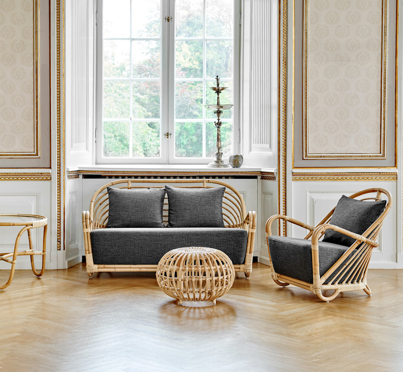 Dies ist ein Lifestyle-Bild von Charlottenborg Sofa in polished Natural Rattan, in einem eleganten klassischen Interieur mit aufwändigen goldenen.