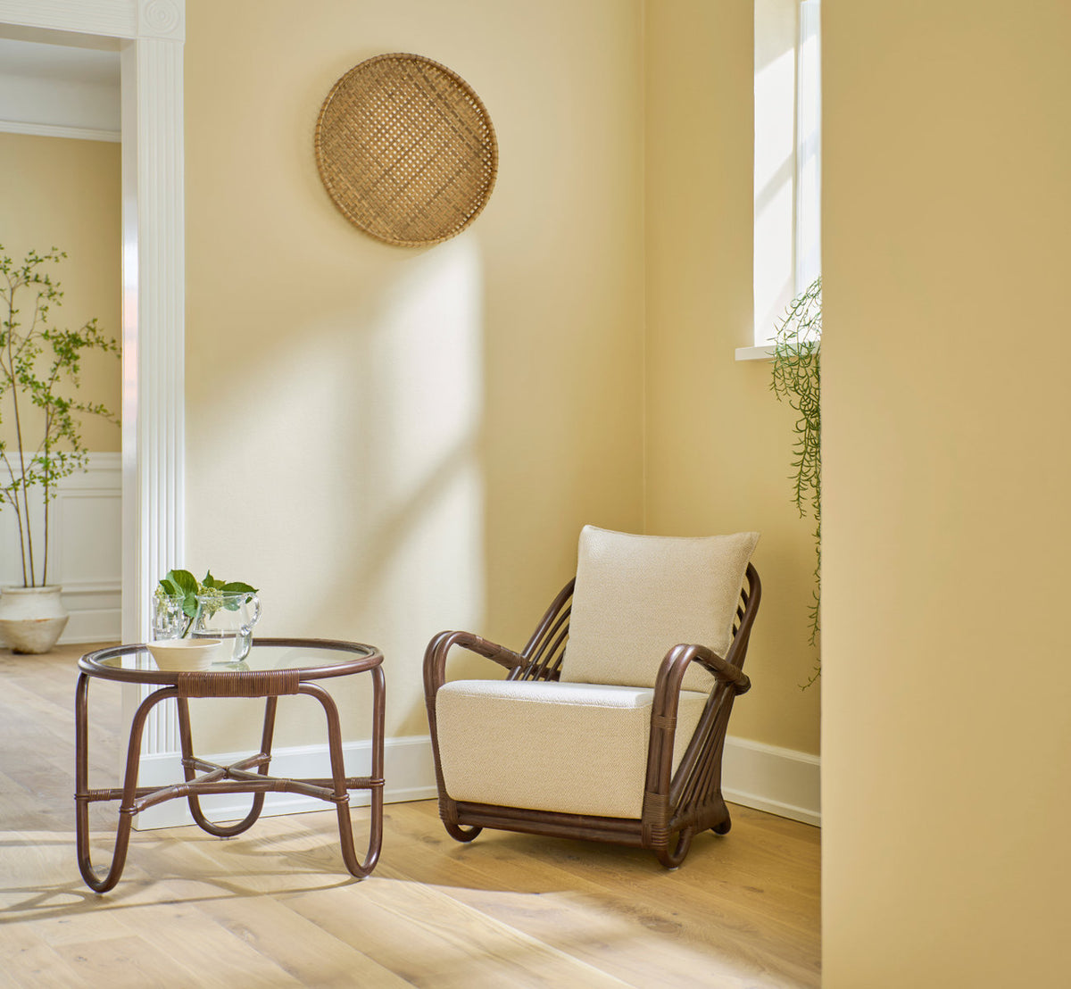 Dies ist ein Lifestyle-Bild von Charlottenborg Couchtisch in brown rattan. Mit Lounge-Sessel in einer warmen gelben Ecke.