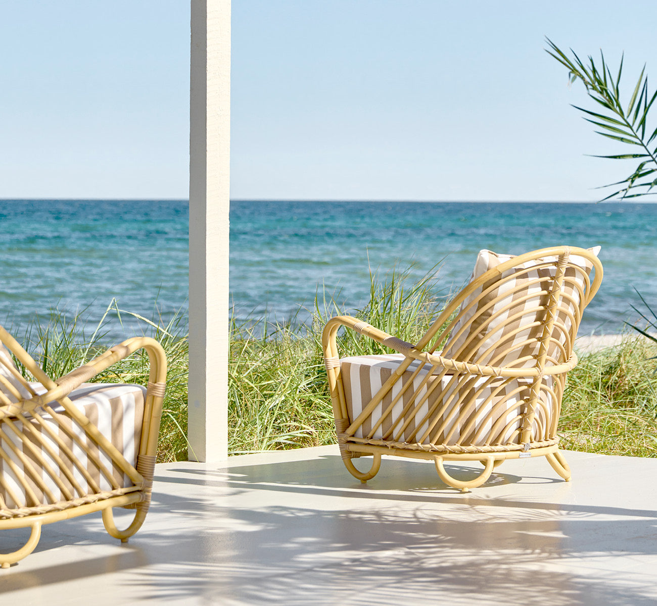 Dies ist ein Lifestyle-Bild von Charlottenborg Außen-Lounge-Sessel in natural Aluminium ArtFibre, auf einer Holzterrasse im Freien mit Blumen und.