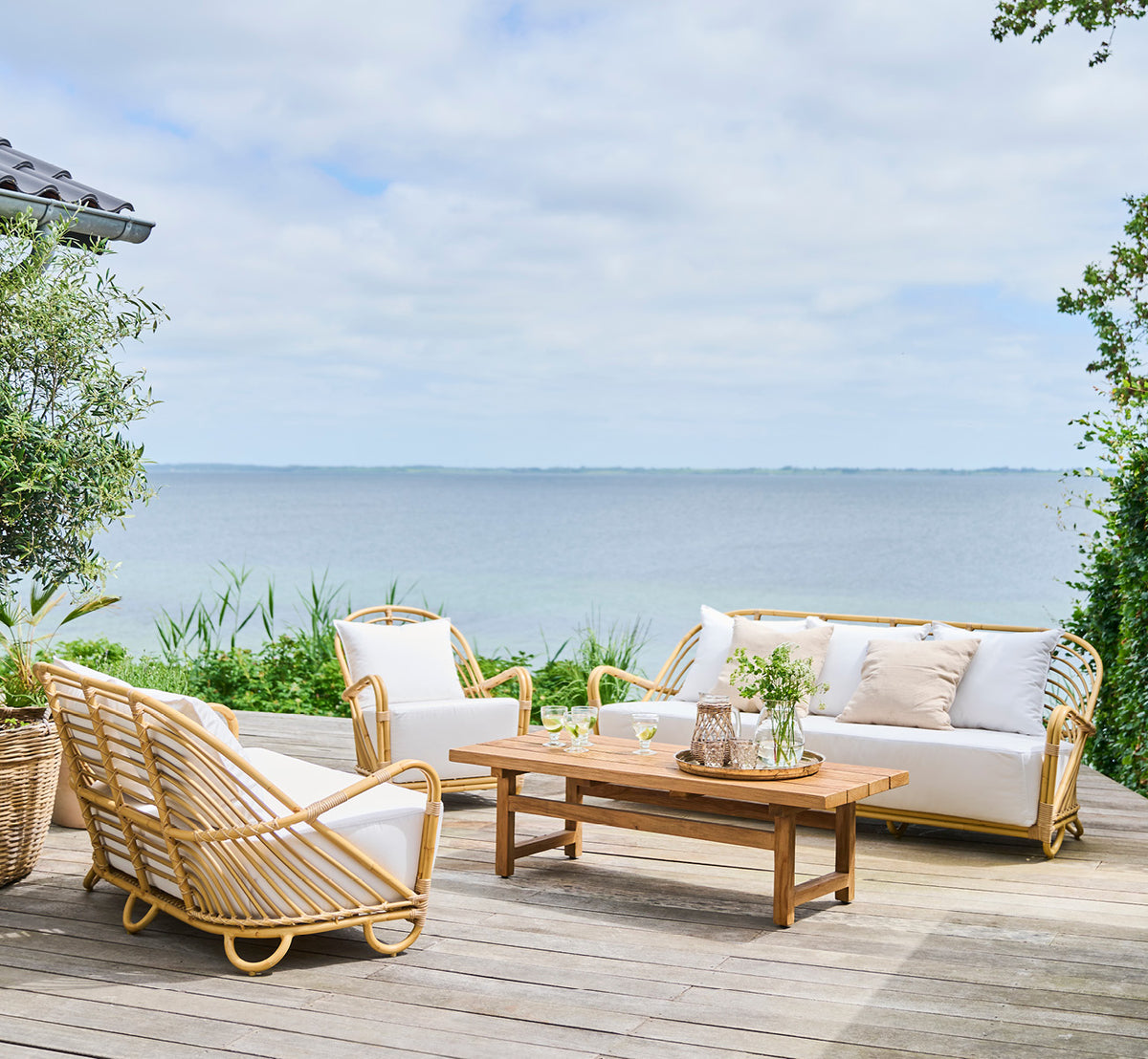 Dies ist ein Lifestyle-Bild von Charlottenborg Außen-Lounge-Sessel in natural Aluminium ArtFibre, auf einer Holzterrasse im Freien mit Blumen und.