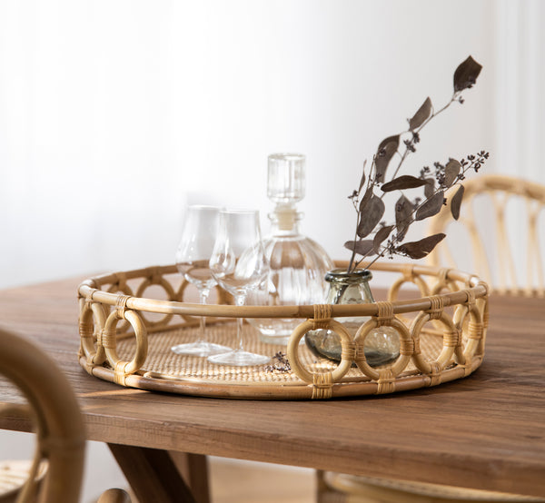 Dies ist ein Lifestyle-Bild von Mira Tray i natural rattan. Auf einem Esstisch mit Glaswaren und getrocknetem Eukalyptus in einem hellen Raum.