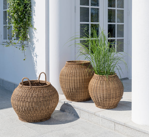 Dies ist ein Lifestyle-Bild von Ellis Korb in chestnut core weave ArtFibre Aluminium, im Freien auf einer sonnigen Terrasse mit weißer Mauer und.