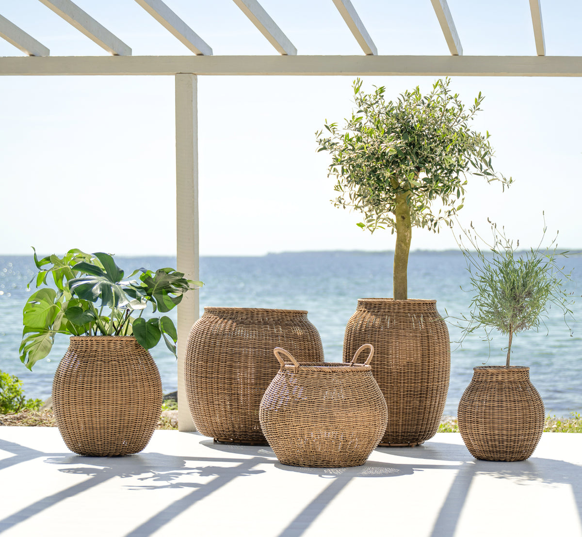Dies ist ein Lifestyle-Bild von Ellis Korb in chestnut core weave ArtFibre Aluminium, im Freien auf einer sonnigen Terrasse mit weißer Mauer und.