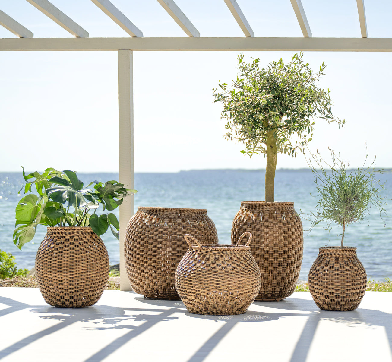 Dies ist ein Lifestyle-Bild von Ellis Korb in chestnut core weave ArtFibre Aluminium, im Freien auf einer sonnigen Terrasse mit weißer Mauer und.