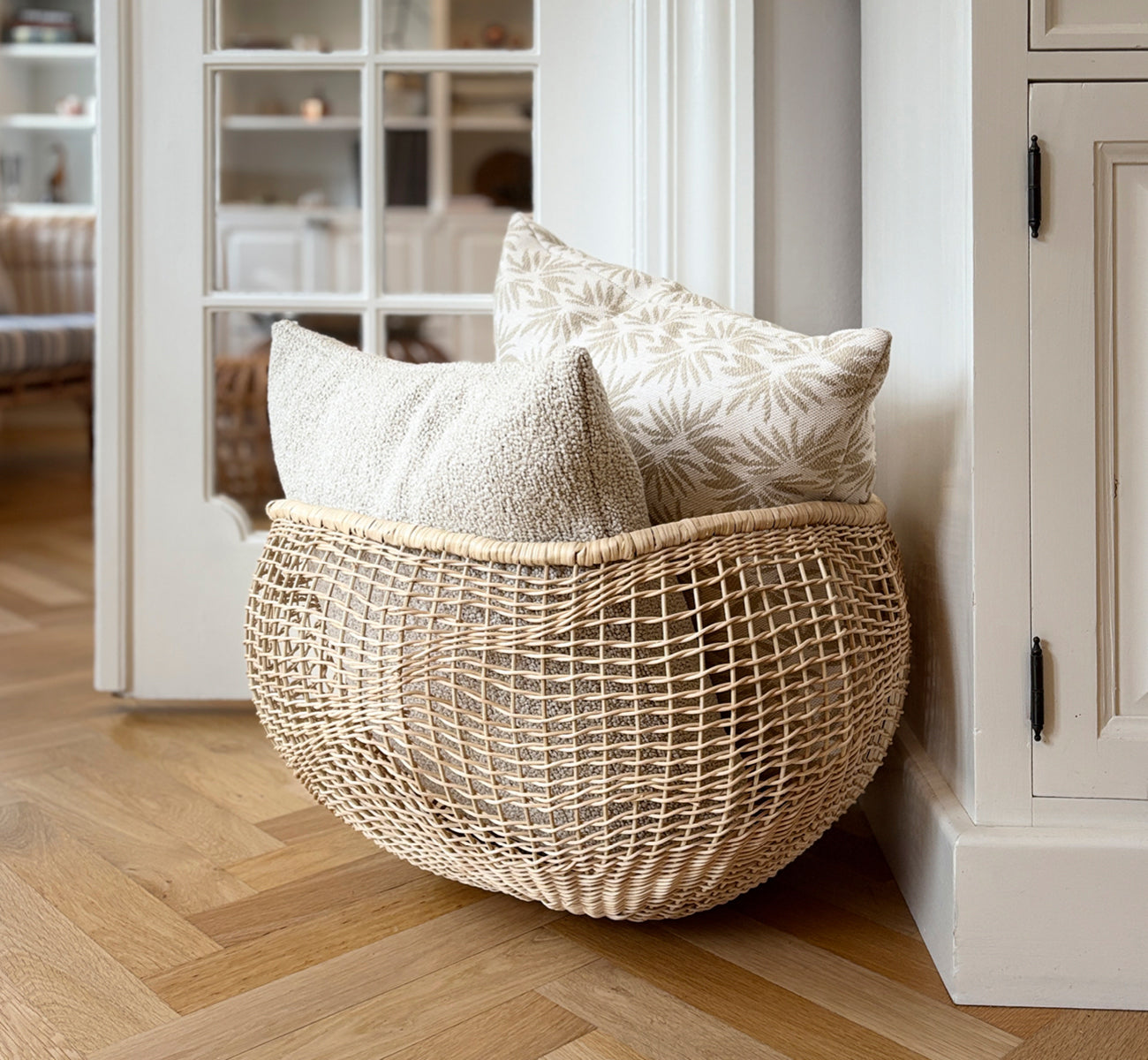 Dies ist ein Lifestyle-Bild von Folia Korb in natural core weave iron frame, in einem hell-weißen Interieur mit Wandvertäfelung, dekoriert mit.