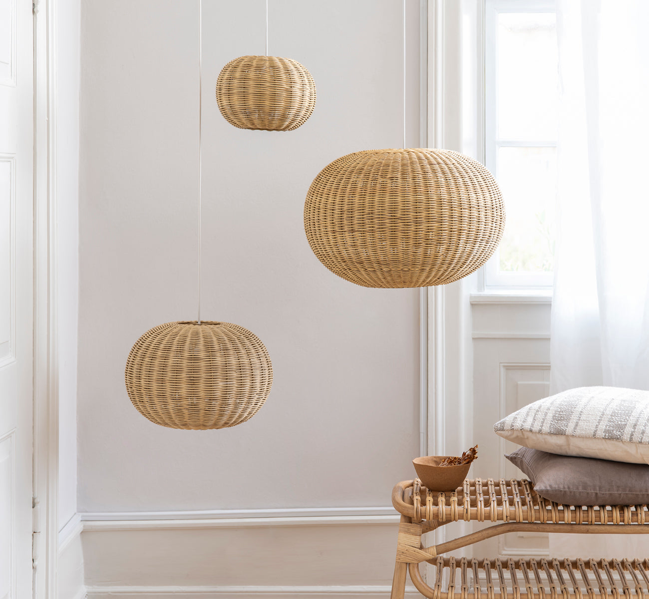 Dies ist ein Lifestyle-Bild von Tangelo Lampshade Ø37 cm | Small in natural rattan. Drei Pendelleuchten über einer Rattanbank in einem hellen Interieur gruppiert.