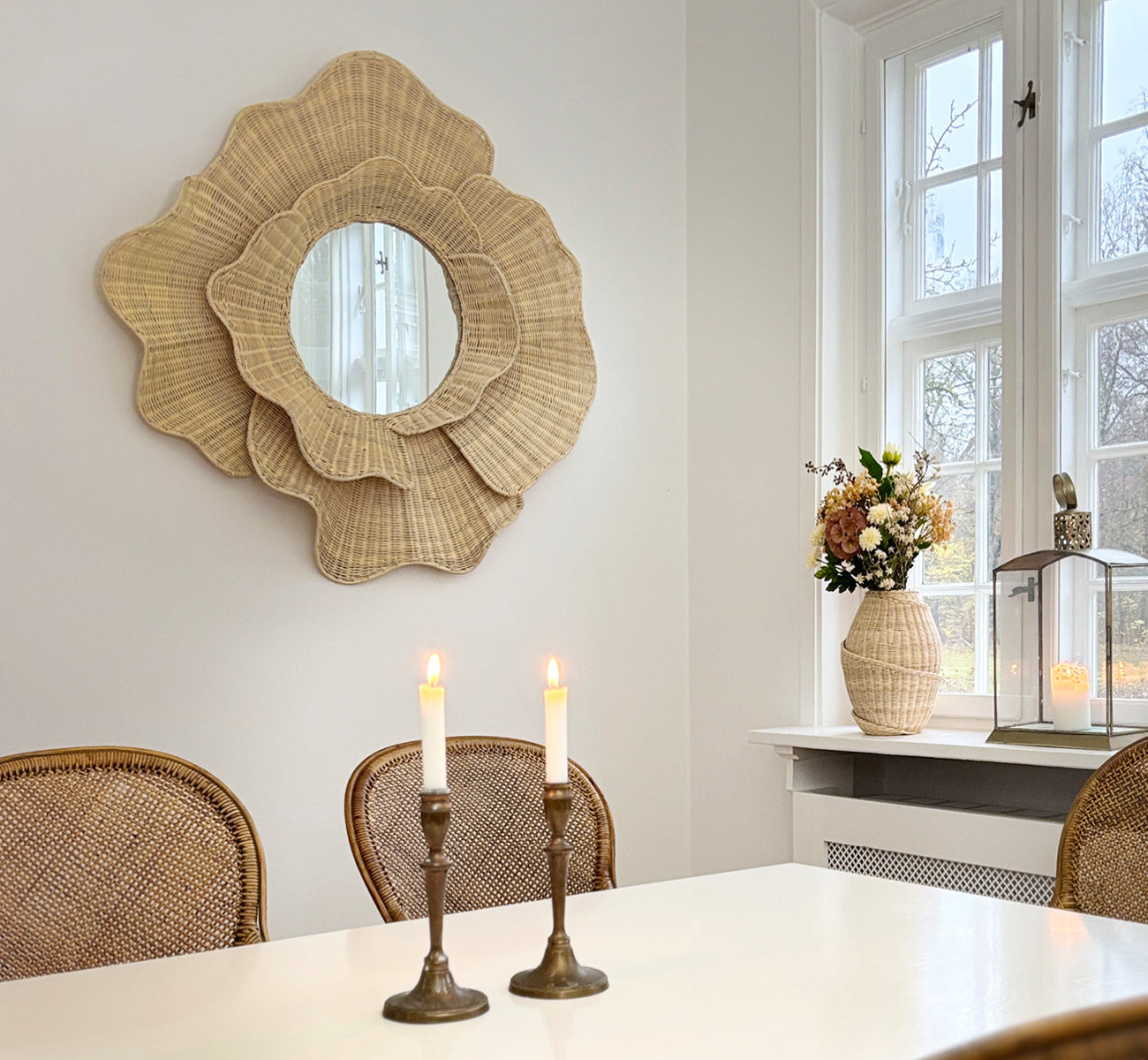Dies ist ein Lifestyle-Bild von Floral Spiegel in natural core weave iron frame, hängend in einem hellen Esszimmer mit Kerzenleuchtern und.