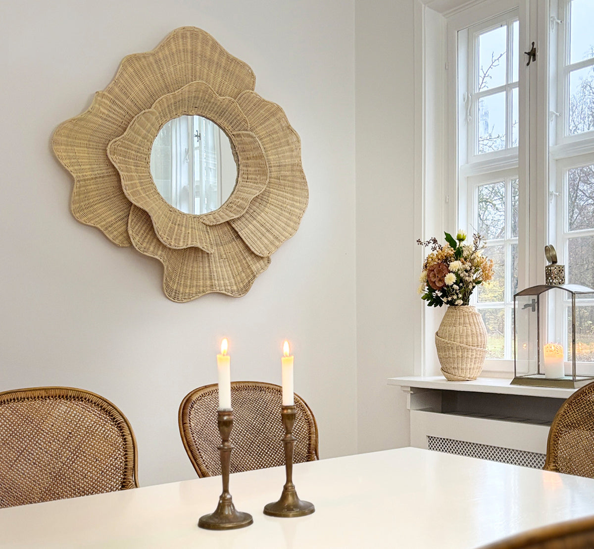 Dies ist ein Lifestyle-Bild von Floral Spiegel in natural core weave iron frame, hängend in einem hellen Esszimmer mit Kerzenleuchtern und.