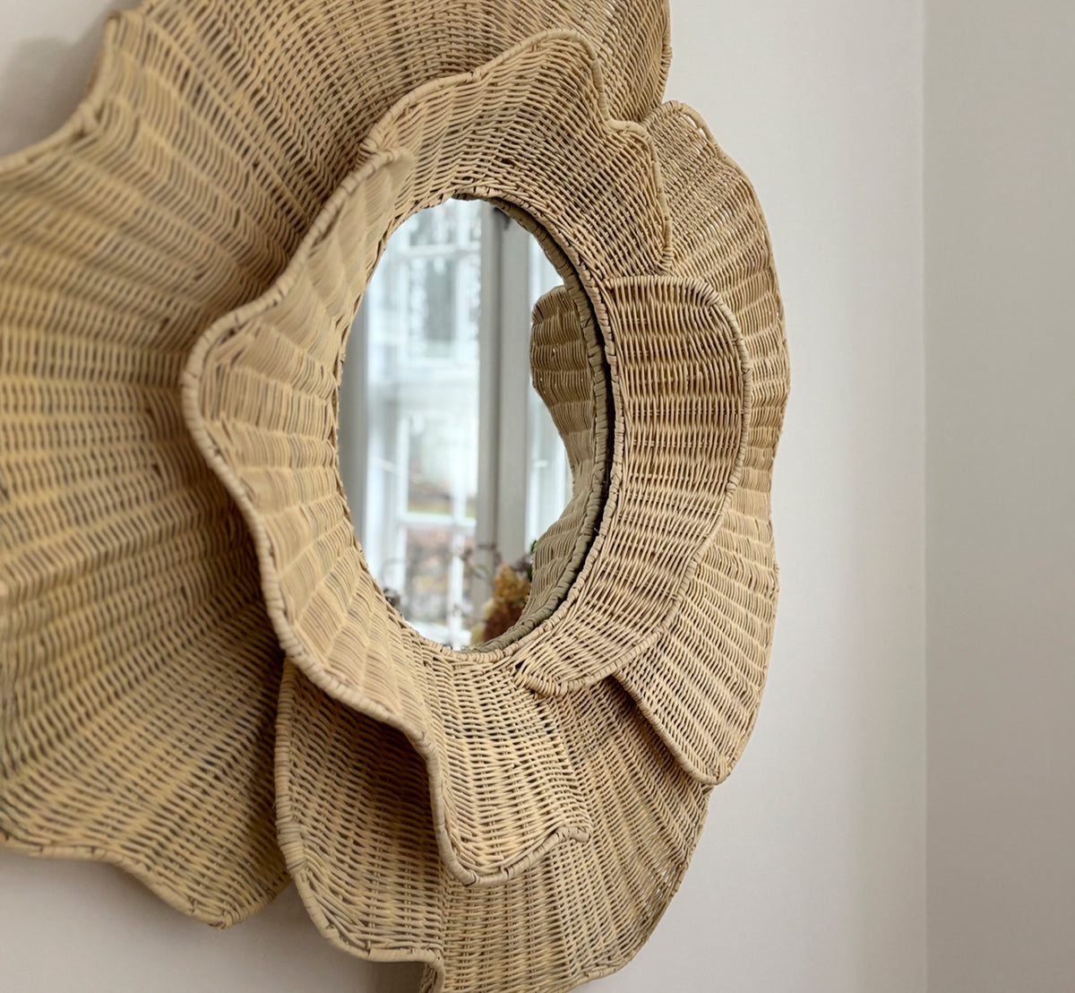 Dies ist ein Lifestyle-Bild von Floral Spiegel in natural core weave iron frame, hängend in einem hellen Esszimmer mit Kerzenleuchtern und.