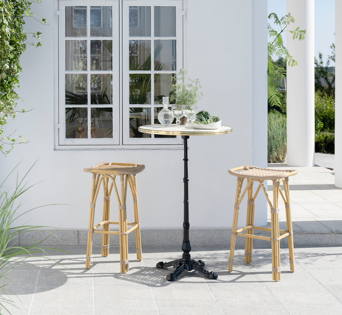 Dies ist ein Lifestyle-Bild von Lyon Bartisch Versalite Marble Ø70 cm in cast iron. Elegante Terrasse mit Barhockern und grünen Pflanzen.