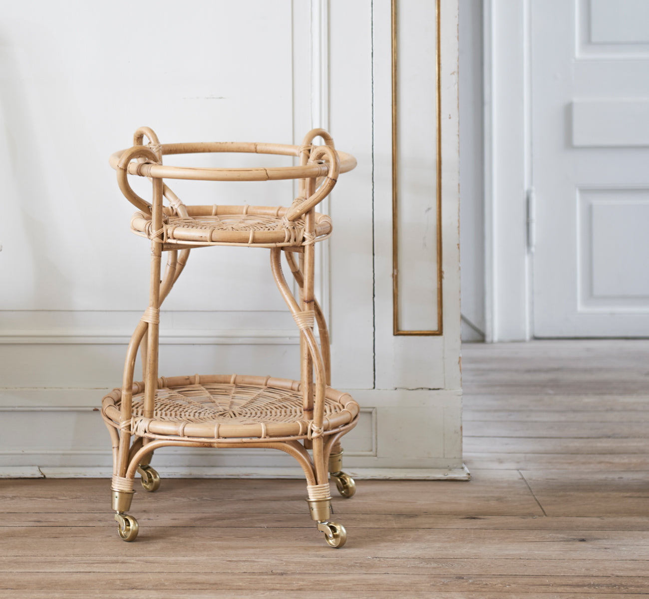 Dies ist ein Lifestyle-Bild von Fratellino Servierwagen in polished Natural Rattan, in einem klassischen Interieur mit aufwändigen weißen Paneeltüren.