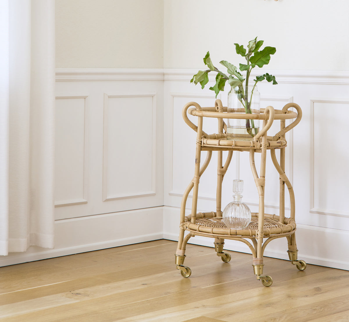 Dies ist ein Lifestyle-Bild von Fratellino Servierwagen in polished Natural Rattan, in einem klassischen Interieur mit aufwändigen weißen Paneeltüren.