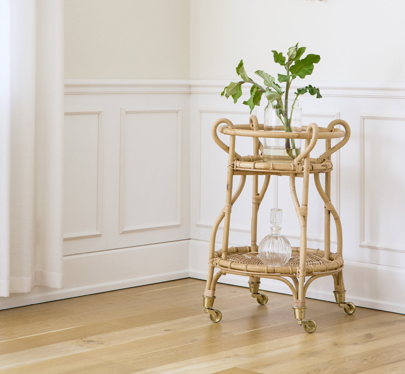 Dies ist ein Lifestyle-Bild von Fratellino Servierwagen in polished Natural Rattan, in einem klassischen Interieur mit aufwändigen weißen Paneeltüren.