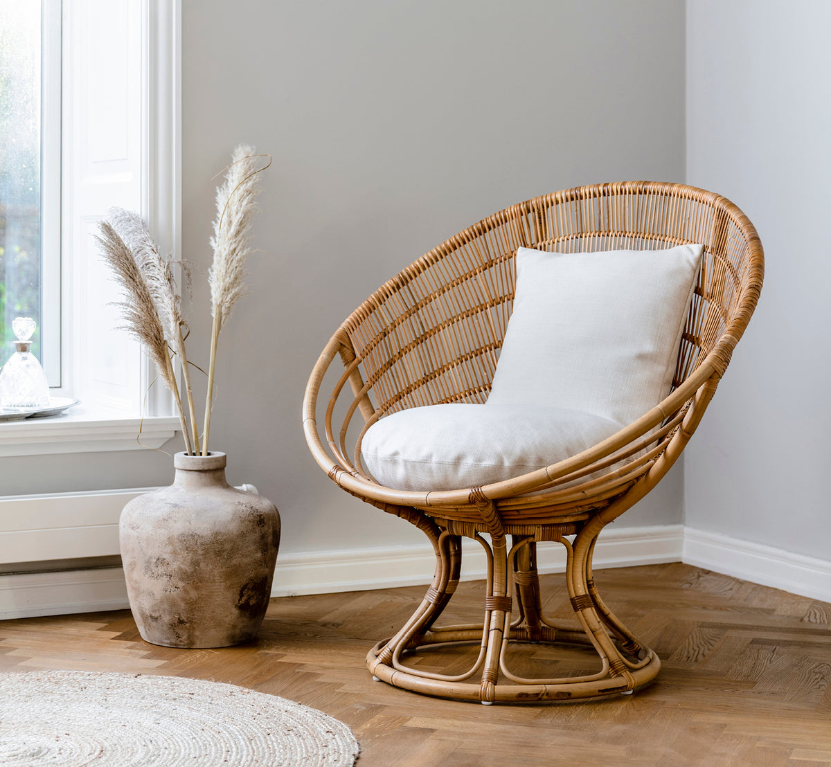 Dies ist ein Lifestyle-Bild von Luna Lounge-Sessel in natural skin on rattan. Mit einem weißen Kissen in einer gemütlichen Ecke mit Pampasgras-Dekoration gestylt.