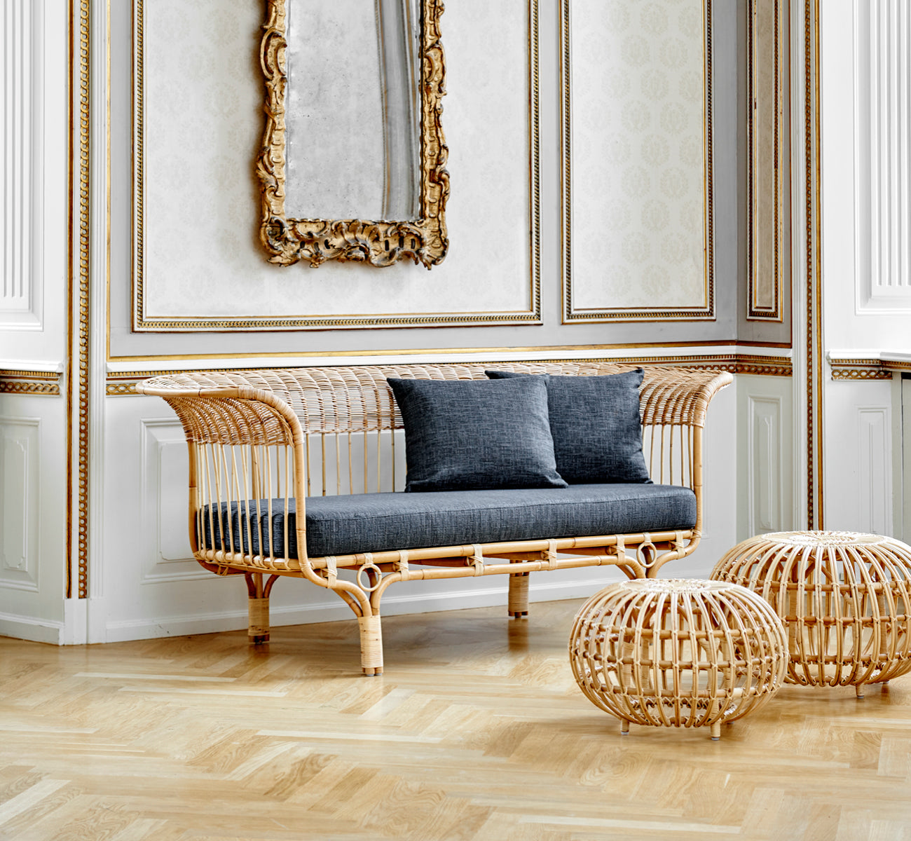 Dies ist ein Lifestyle-Bild von Ottoman Small in natural skin on rattan. In einem klassisch vertäfelten Interieur mit einer antiken Uhr gruppiert.
