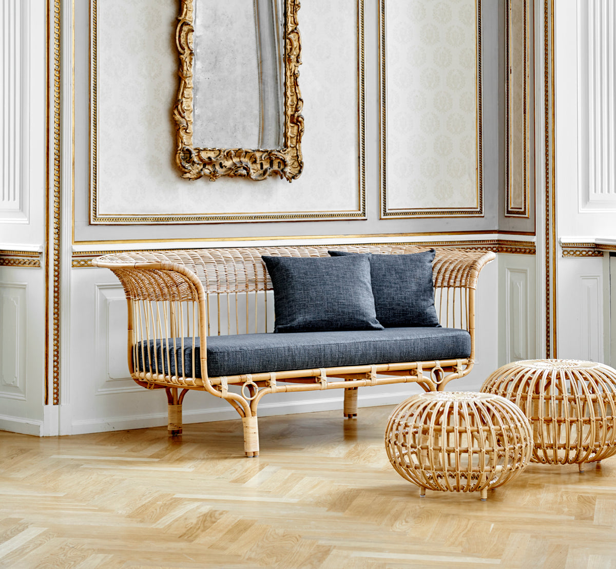 Dies ist ein Lifestyle-Bild von Ottoman Small in natural skin on rattan. In einem klassisch vertäfelten Interieur mit einer antiken Uhr gruppiert.
