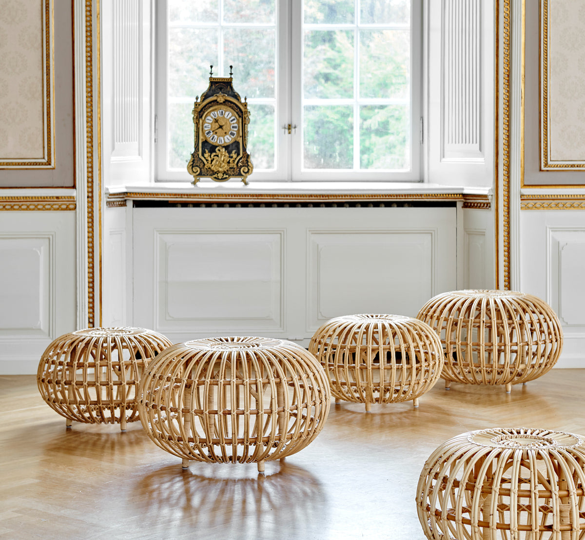 Dies ist ein Lifestyle-Bild von Ottoman Large in natural skin on rattan. In einem klassisch vertäfelten Interieur mit einer vergoldeten Uhr gruppiert.