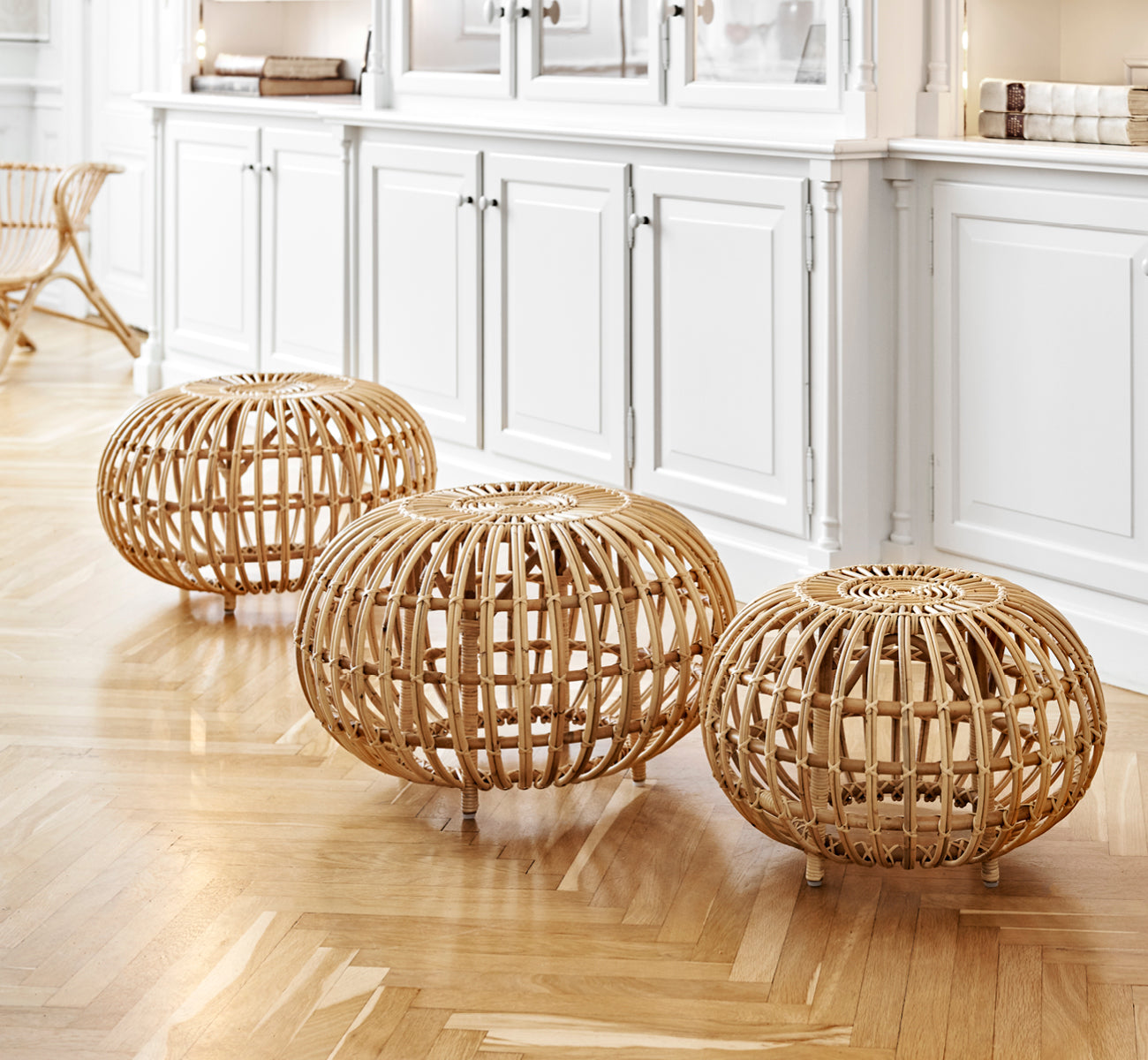 Dies ist ein Lifestyle-Bild von Ottoman Large in natural skin on rattan. In einem klassisch vertäfelten Interieur mit einer vergoldeten Uhr gruppiert.