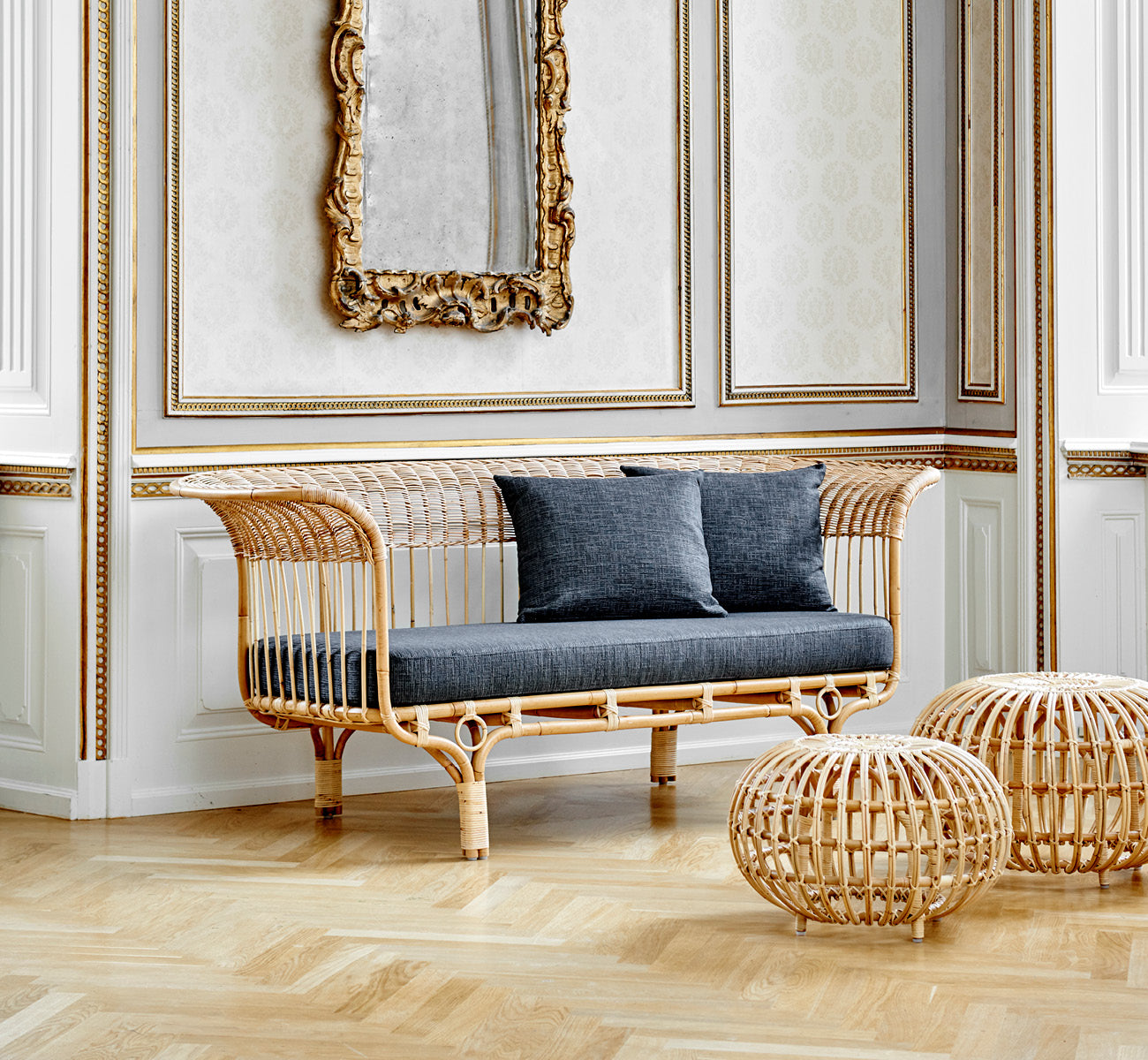 Dies ist ein Lifestyle-Bild von Belladonna Sofa in polished natural rattan, in einem hellen skandinavischen Interieur durch einen weißen Türrahmen.