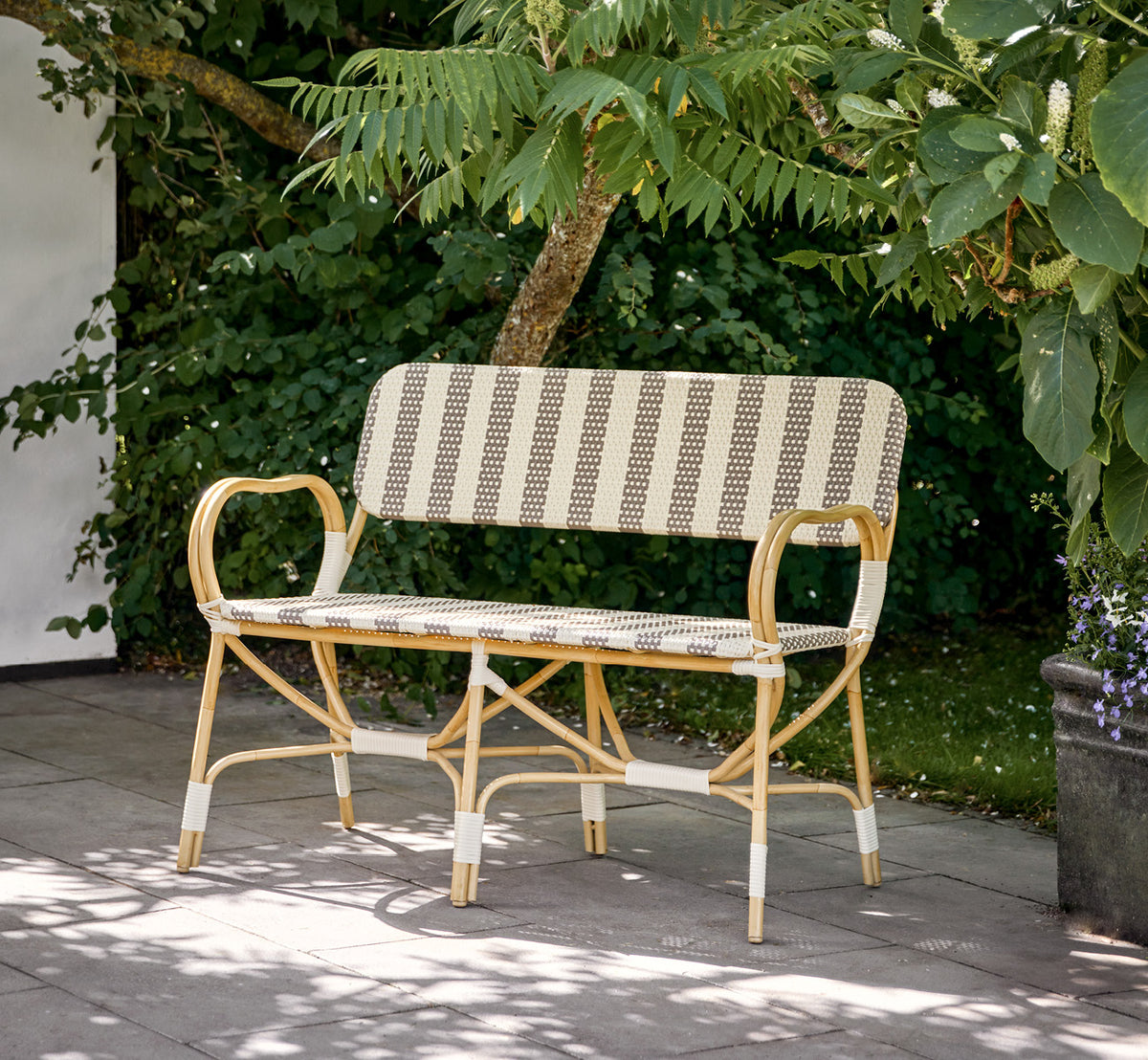 Dies ist ein Lifestyle-Bild von Bistro Exterior Bank in natural Aluminium ArtFibre, in einem Gartencafé im Freien mit einem Bistrotisch und.