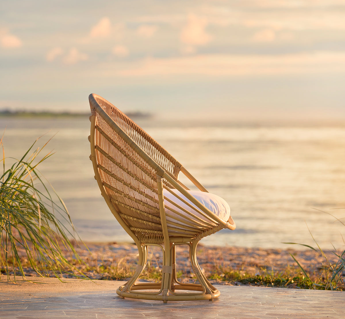 Dies ist ein Lifestyle-Bild von Luna Außen-Lounge-Sessel in natural aluminium artfibre. Am Ufer bei goldenem Sonnenuntergang mit dem Meer dahinter platziert.