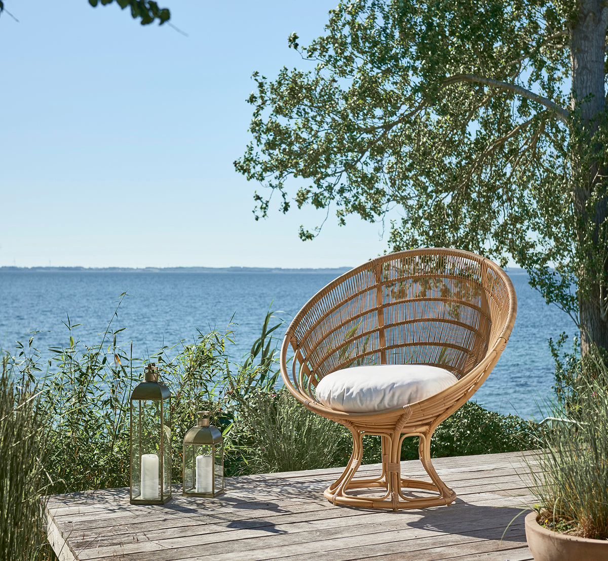 Dies ist ein Lifestyle-Bild von Luna Außen-Lounge-Sessel in natural aluminium artfibre. Auf einem Holzdeck am Meer, umgeben von üppigem Grün.