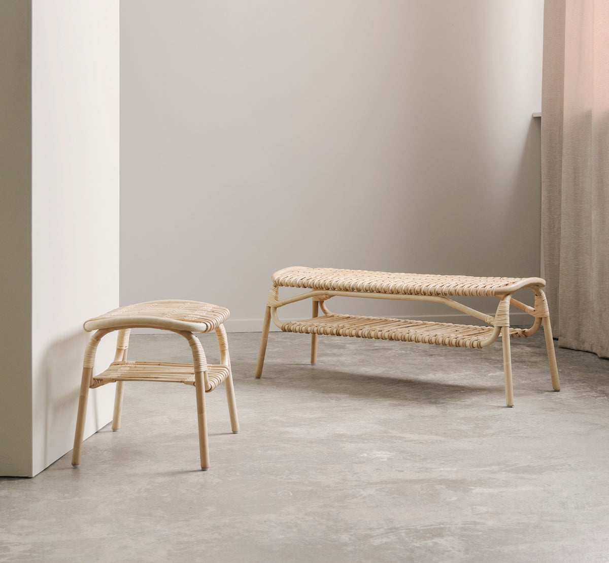 Dies ist ein Lifestyle-Bild von Machiya Hocker in natural skin on rattan. Minimaler Raum mit Betonboden, Rattanbank und Leinenvorhang.