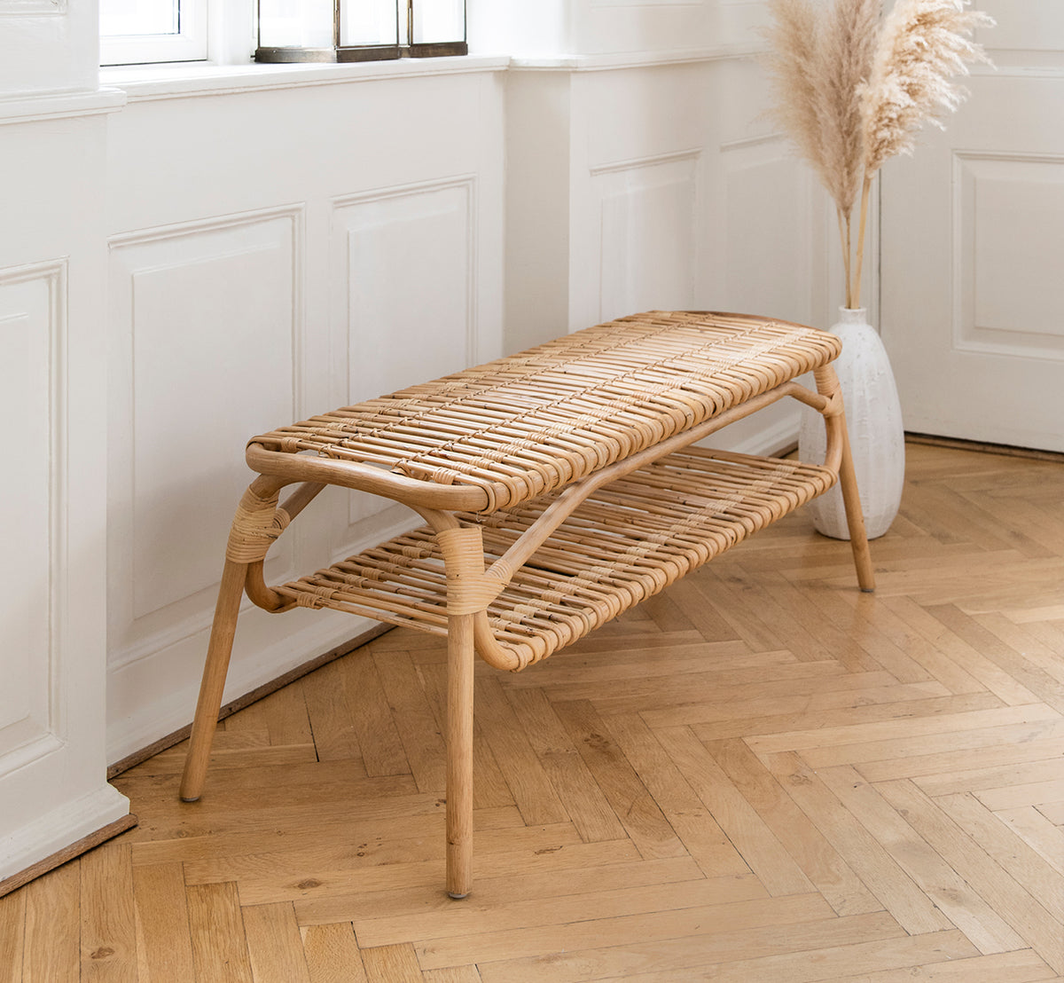 Dies ist ein Lifestyle-Bild von Machiya Bank in natural skin on rattan. Weiß vertäfelter Flur mit Fischgrätboden und Pampasgras-Vase.