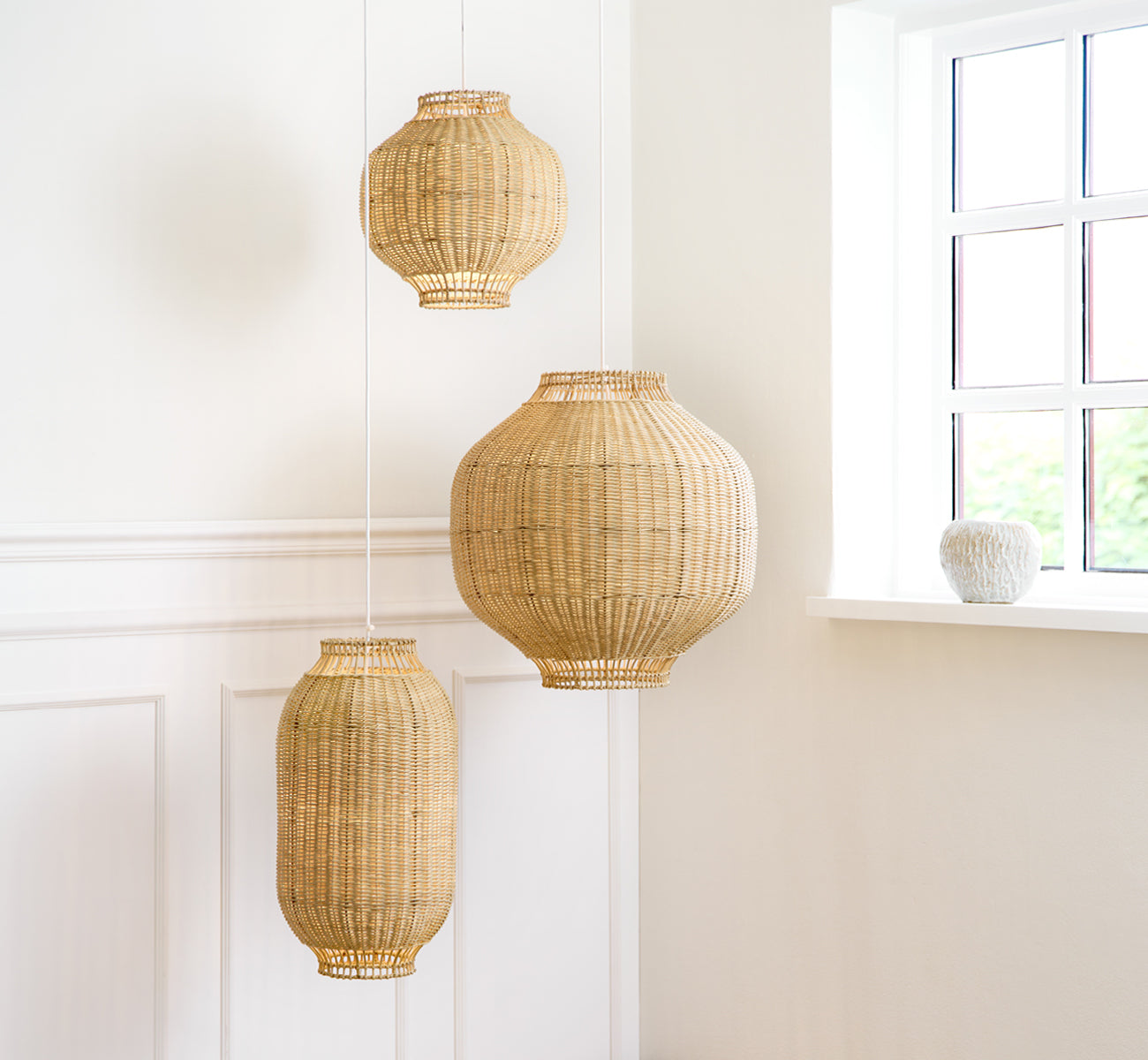 Dies ist ein Lifestyle-Bild von Tomori Lampenschirm in natural core weave rattan frame. Die größte von drei Pendelleuchten in einem hellen vertäfelten Raum.