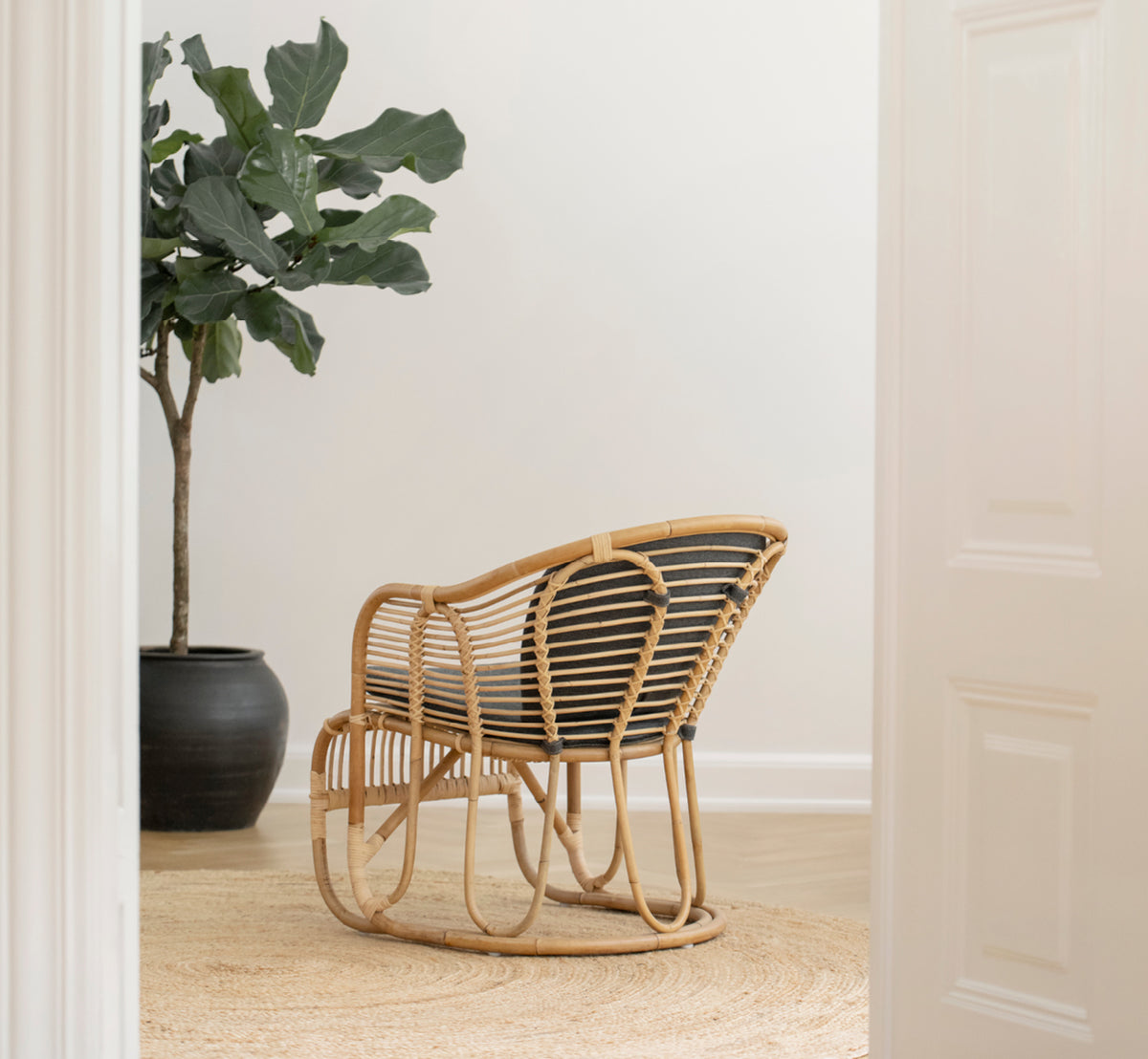 Dies ist ein Lifestyle-Bild von Swing Lounge-Sessel in polished natural rattan. Allein neben einer Grünpflanze auf einem Fischgrätparkettboden stehend.
