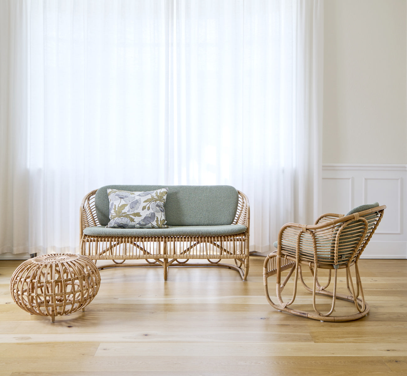 Dies ist ein Lifestyle-Bild von Swing Lounge-Sessel in polished natural rattan. Allein neben einer Grünpflanze auf einem Fischgrätparkettboden stehend.