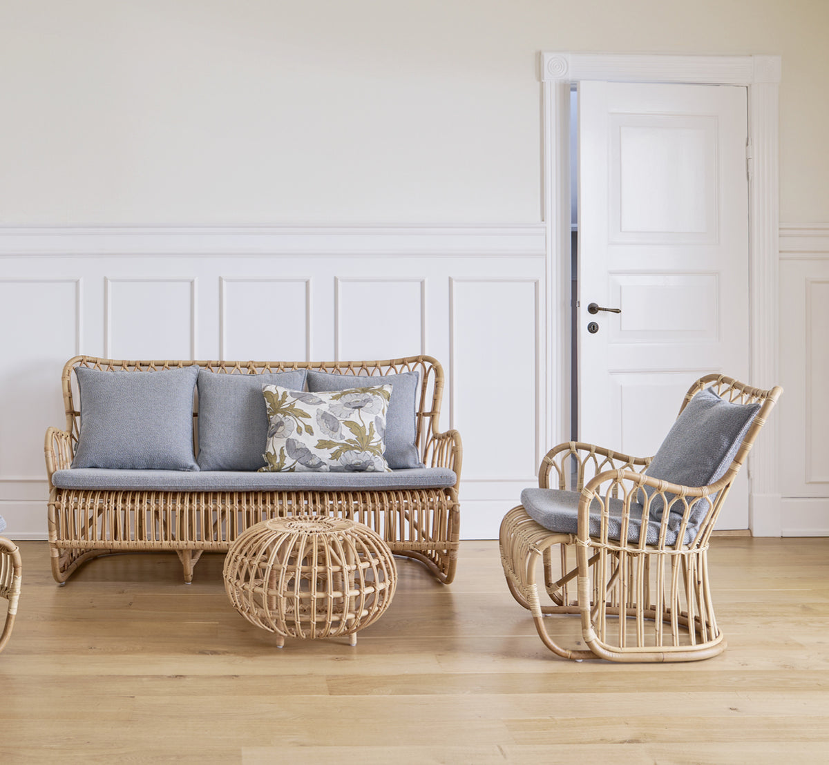 Dies ist ein Lifestyle-Bild von Tulip Sofa in polished natural rattan. Mit einem Rattan-Loungesessel an einem sonnigen Vorhangfenster kombiniert.