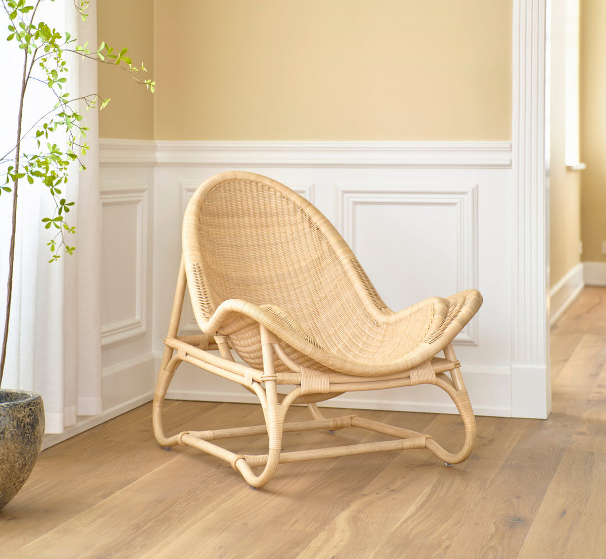 Dies ist ein Lifestyle-Bild von Pacifique Lounge-Sessel in natural core weave rattan frame. Vor weißen Paneelen und einer Topfpflanze.