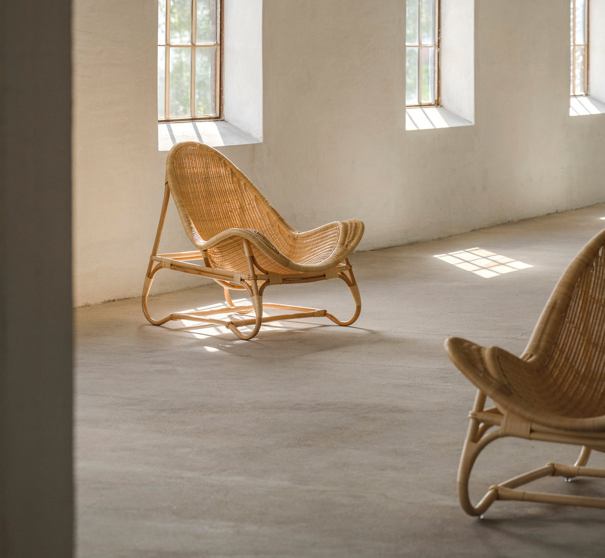 Dies ist ein Lifestyle-Bild von Pacifique Lounge-Sessel in natural core weave rattan frame. Paar in einem sonnigen Raum mit Betonboden.