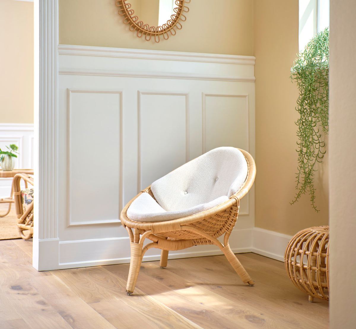 Dies ist ein Lifestyle-Bild von Rana Lounge-Sessel in natural core weave rattan frame. Mit weißem Kissen vor Paneelen und einer Pflanze.