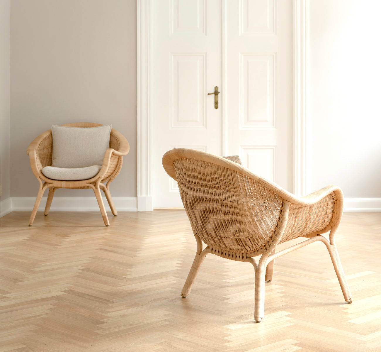 Dies ist ein Lifestyle-Bild von Madame Lounge-Sessel in natural core weave rattan frame. Heller Raum mit Fischgrätboden und weißen Doppeltüren.