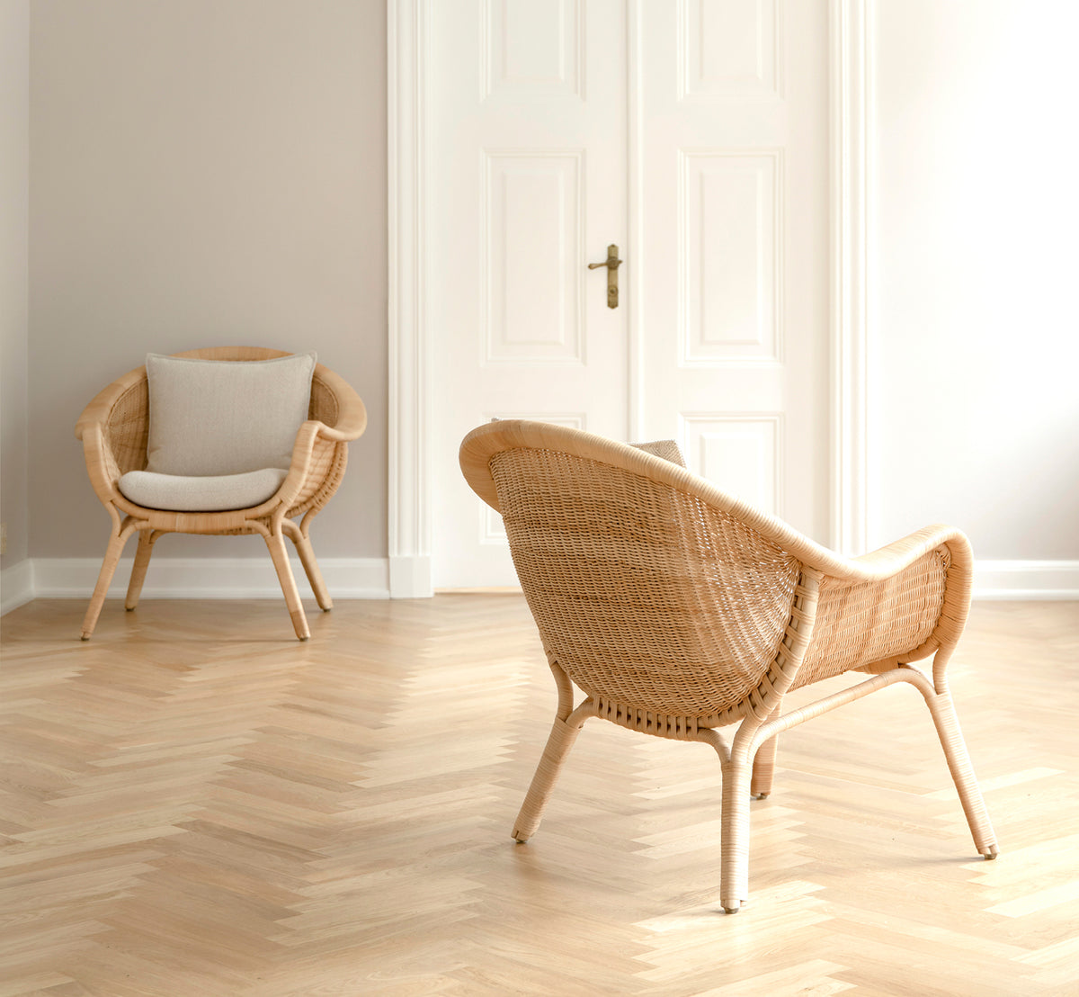Dies ist ein Lifestyle-Bild von Madame Lounge-Sessel in natural core weave rattan frame. Heller Raum mit Fischgrätboden und weißen Doppeltüren.