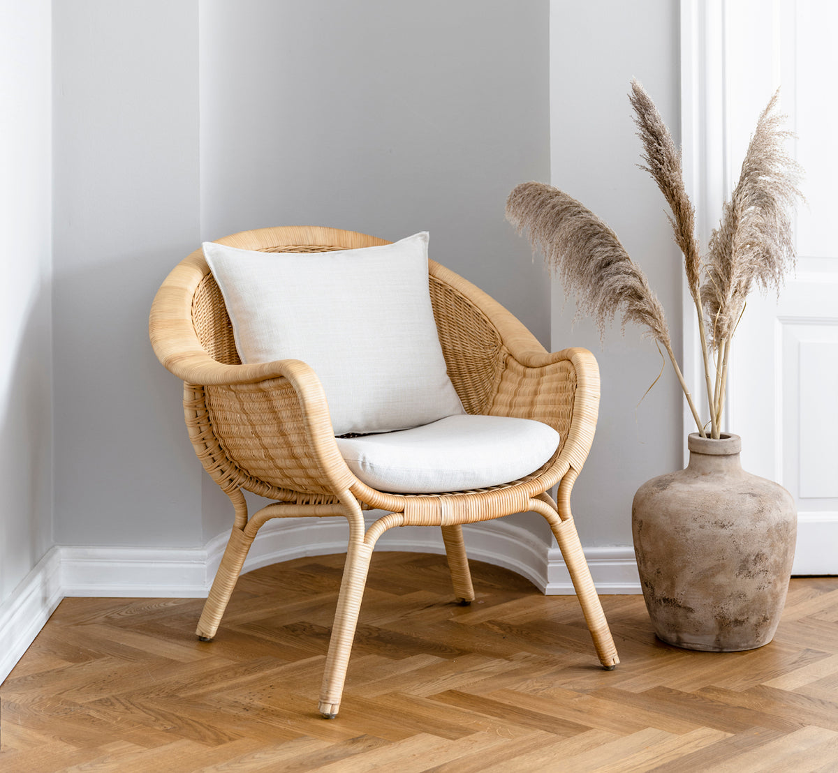 Dies ist ein Lifestyle-Bild von Madame Lounge-Sessel in natural core weave rattan frame. Gemütliche Ecke mit Fischgrätboden und Pampasgras-Vase.