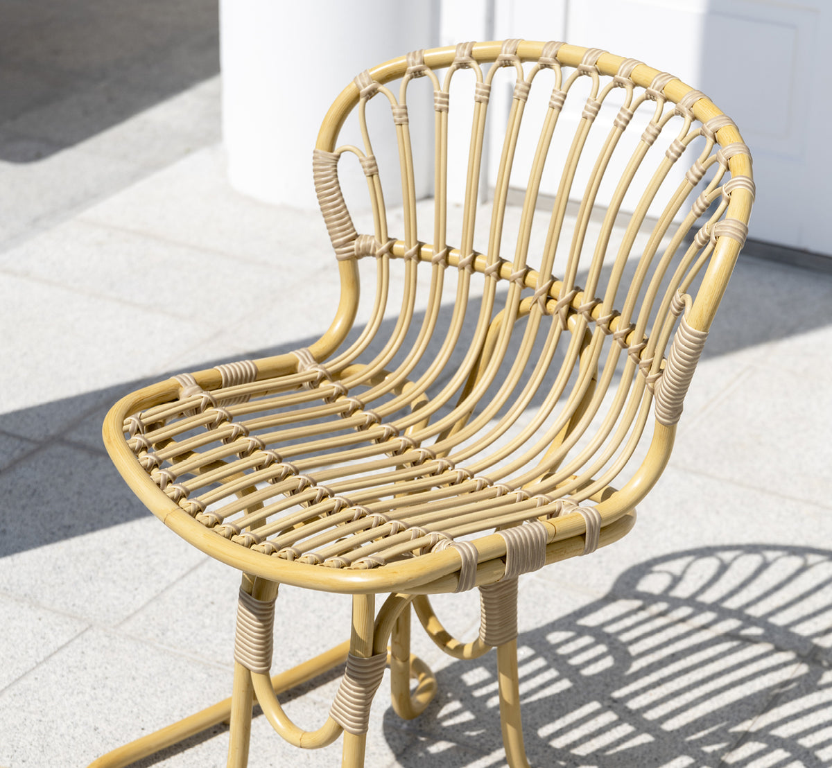 Dies ist ein Lifestyle-Bild von Rita Außen-Esszimmerstuhl in natural aluminium artfibre. Mit einem Bistrotisch auf einer weißen Kolonnadenterrasse kombiniert.
