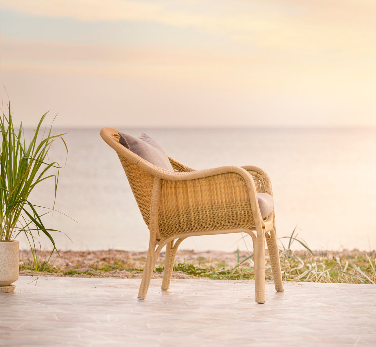 Dies ist ein Lifestyle-Bild von Madame Lounge-Sessel in natural core weave ArtFibre Aluminium, auf einer offenen Küstenterrasse bei Sonnenuntergang.