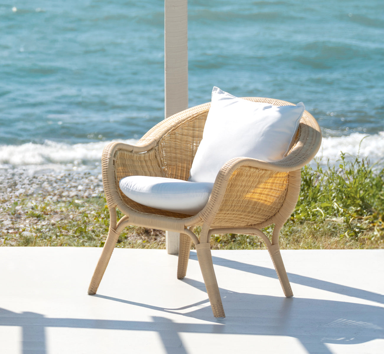 Dies ist ein Lifestyle-Bild von Madame Lounge-Sessel in natural core weave ArtFibre Aluminium, auf einer offenen Küstenterrasse bei Sonnenuntergang.