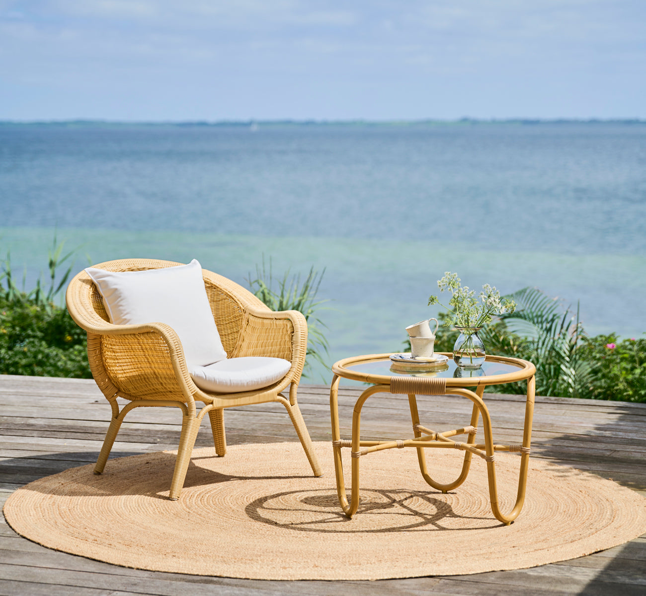 Dies ist ein Lifestyle-Bild von Madame Lounge-Sessel in natural core weave ArtFibre Aluminium, auf einer offenen Küstenterrasse bei Sonnenuntergang.