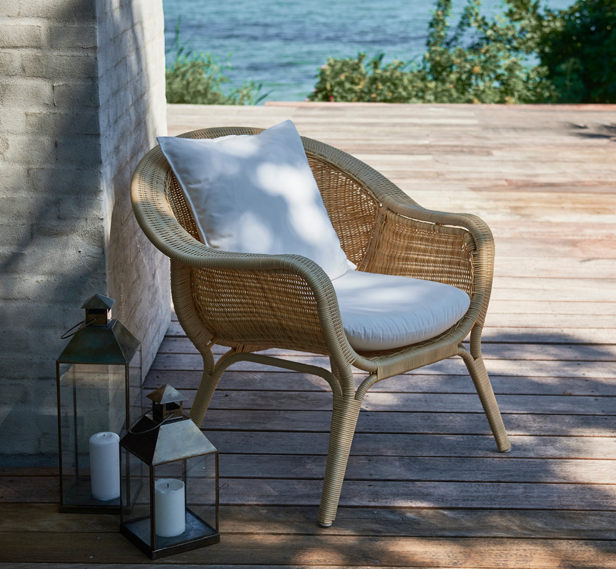 Dies ist ein Lifestyle-Bild von Madame Lounge-Sessel in natural core weave ArtFibre Aluminium, auf einer offenen Küstenterrasse bei Sonnenuntergang.