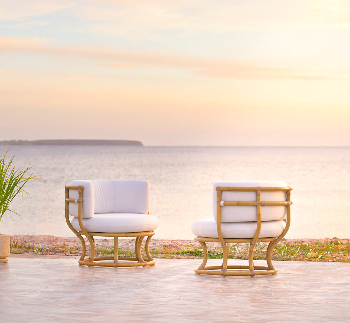 Dies ist ein Lifestyle-Bild von Coco Außen-Lounge-Sessel in natural Aluminium ArtFibre, auf einer offenen Küstenterrasse bei Sonnenuntergang mit.