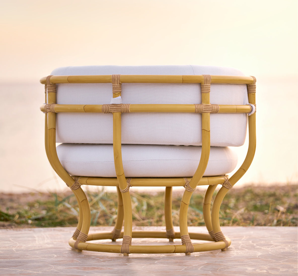 Dies ist ein Lifestyle-Bild von Coco Außen-Lounge-Sessel in natural Aluminium ArtFibre, auf einer offenen Küstenterrasse bei Sonnenuntergang mit.