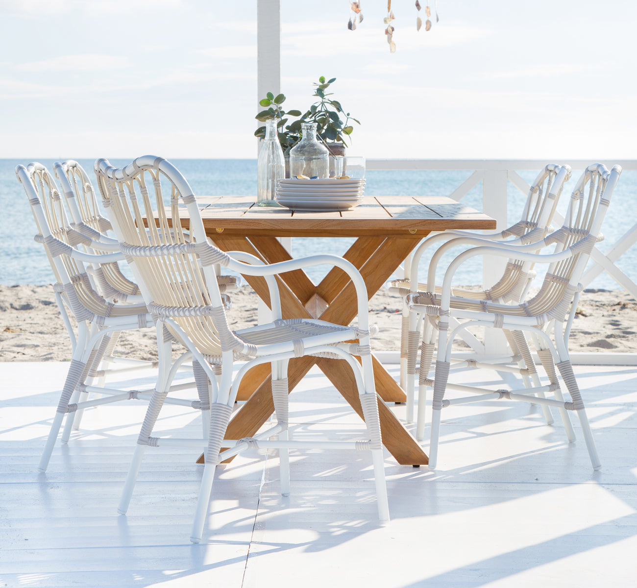 Dies ist ein Lifestyle-Bild von Margret Außen-Esszimmer-Armlehnstuhl in dove white aluminium artfibre. Strandterrasse mit Teaktisch und Dekorationen.