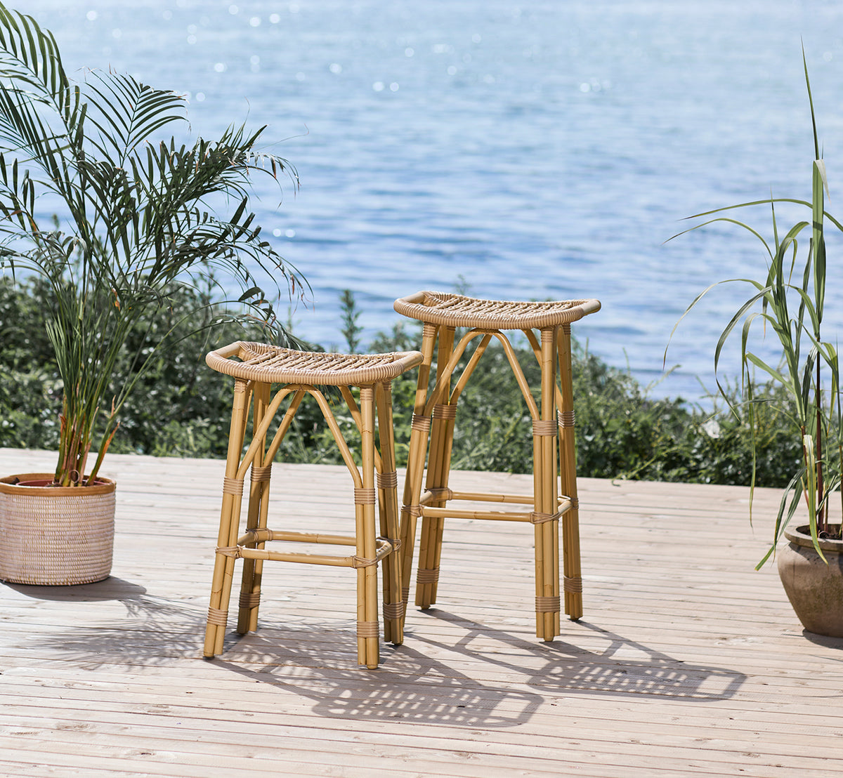 Dies ist ein Lifestyle-Bild von Salsa Außen-Barhocker in natural aluminium artfibre. Uferterrasse mit Palmen und Meerblick.